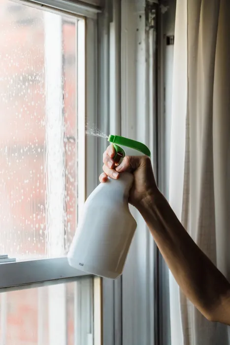 Close-up of a spray bottle cleaning a glass window indoors