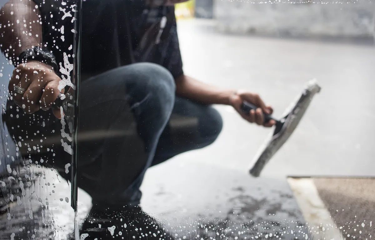 Person cleaning indoor glass windows with a yellow cloth